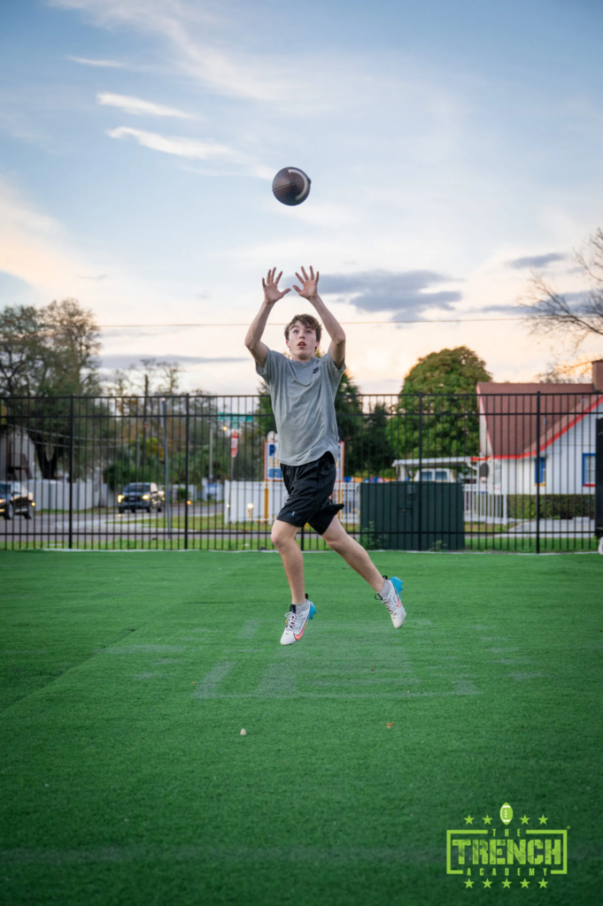 Young athlete jumping to catch a football during outdoor Trench Academy training